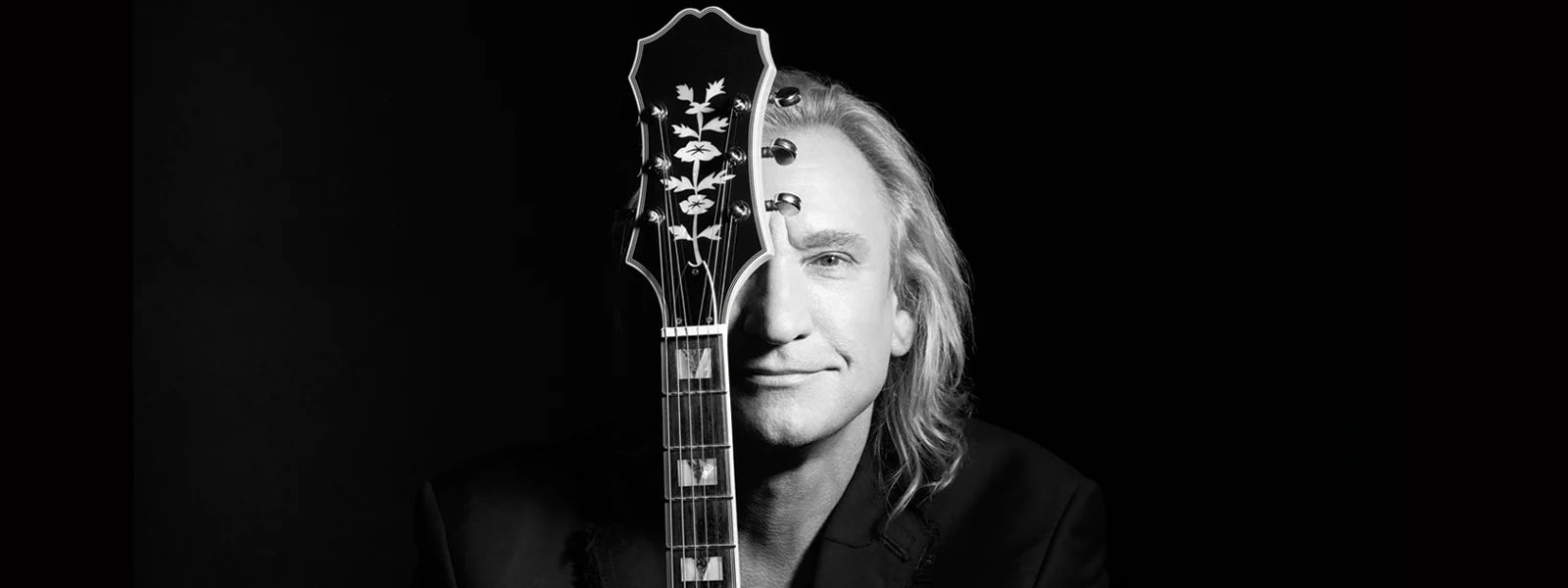 Black and white photo of Joe Walsh posing with guitar, smiling